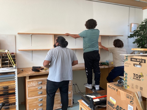 3 personen helpen met het plaatsen van boekenplanken