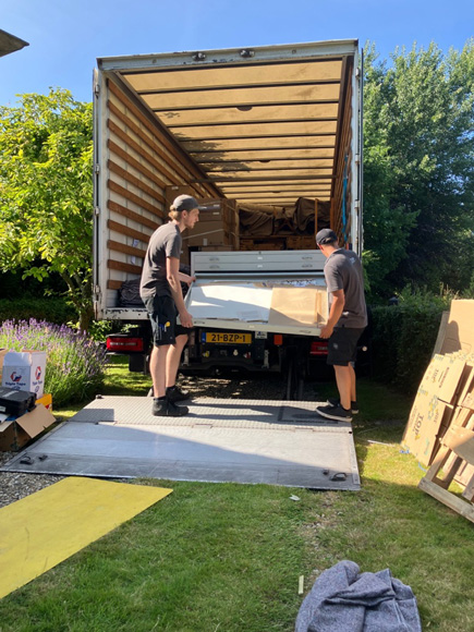 twee mannen schuiven de zware kast in een verhuiswagen